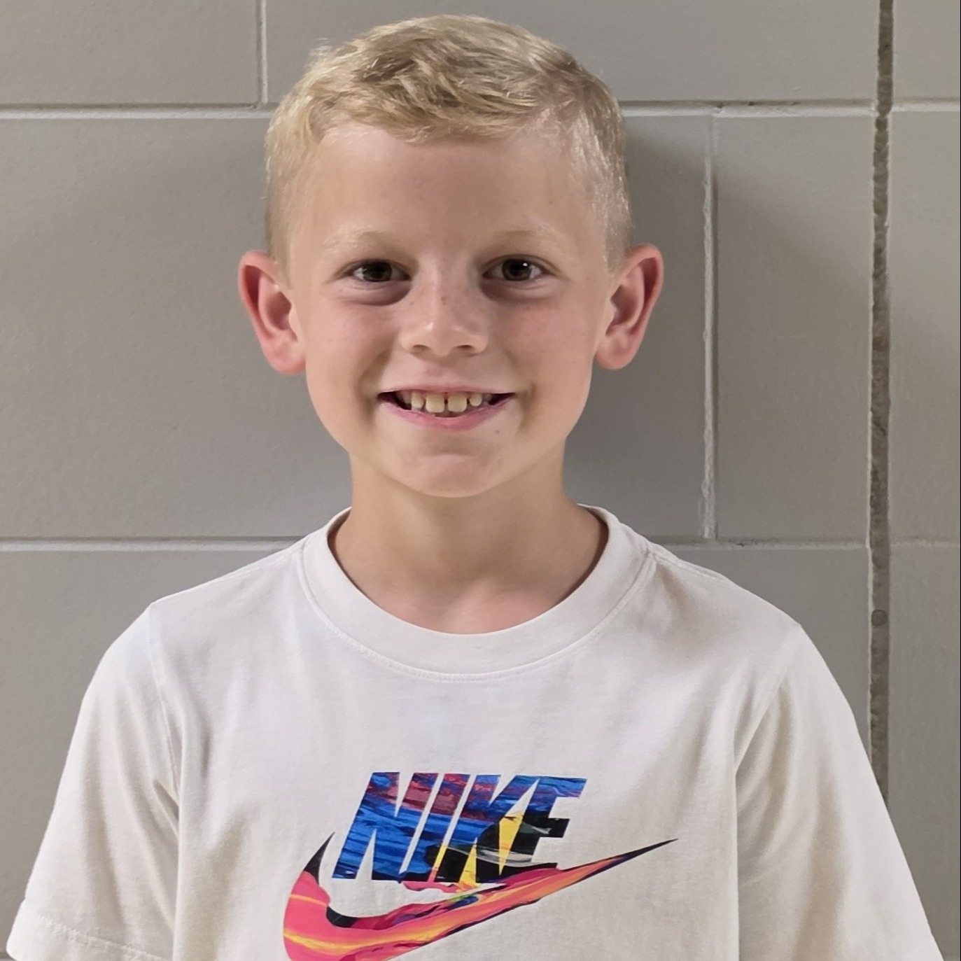 smiling boy with blonde hair wearing a white Nike t-shirt