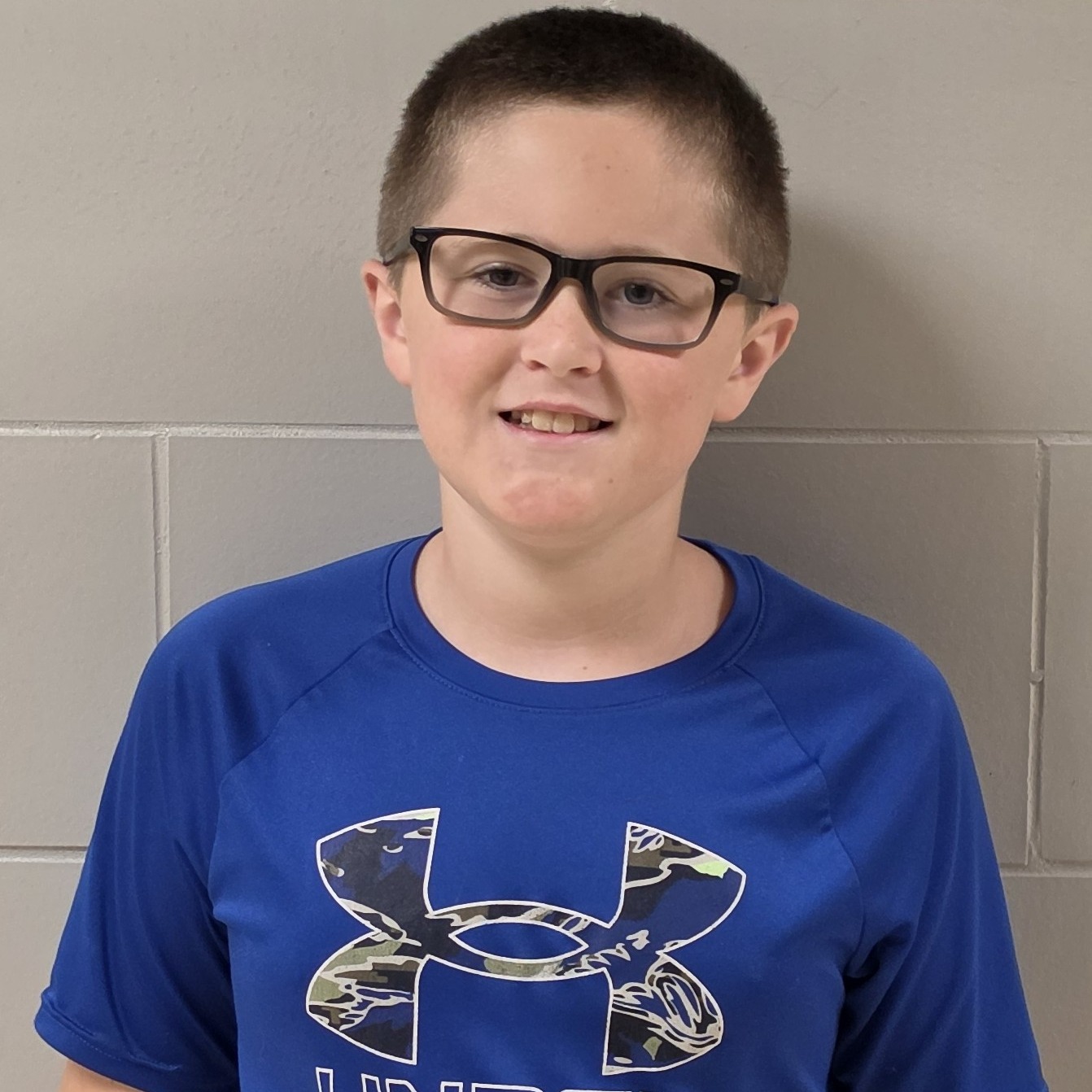 smiling boy with brown hair and glasses wearing a blue UnderArmour t-shirt