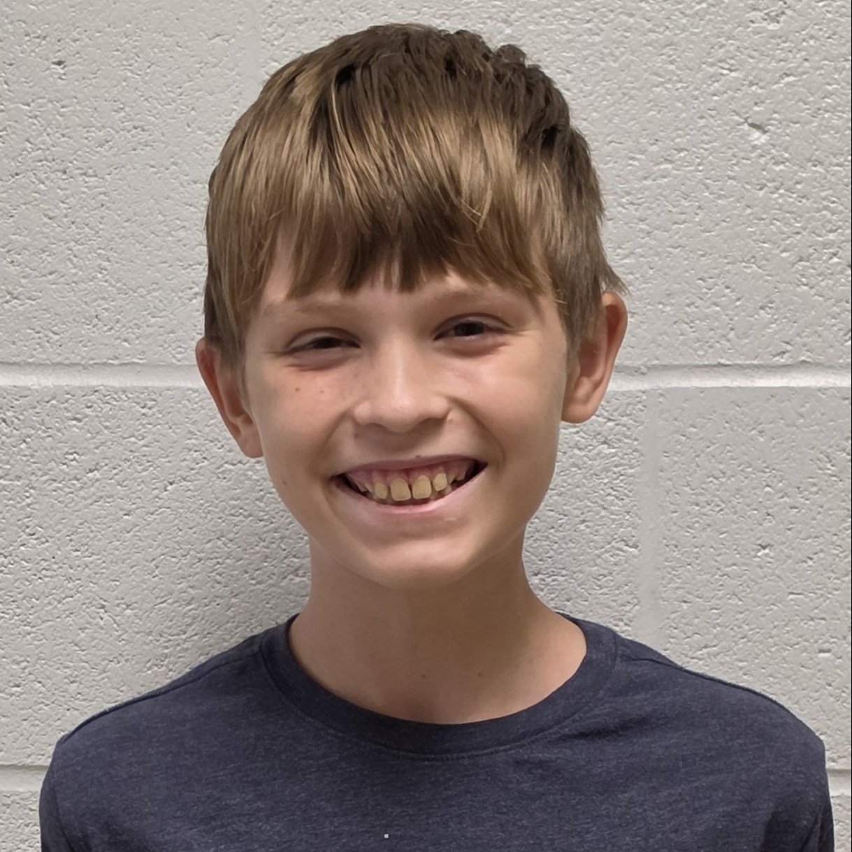 smiling boy with light brown hair wearing a navy blue t-shirt