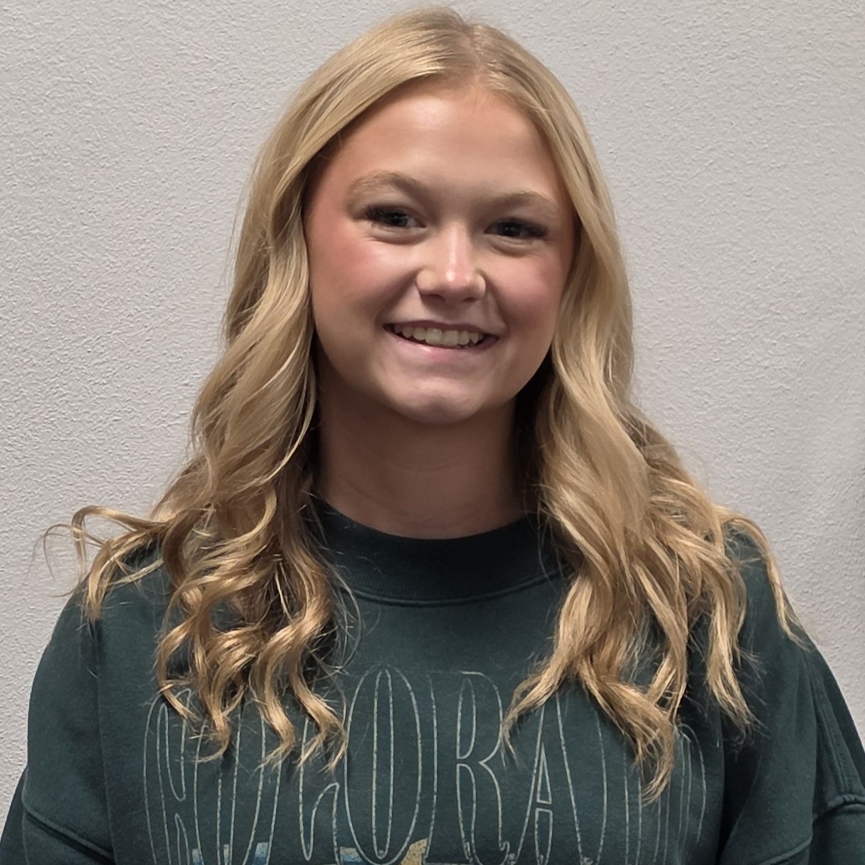 smiling young lady with long, blonde hair wearing a dark green sweatshirt