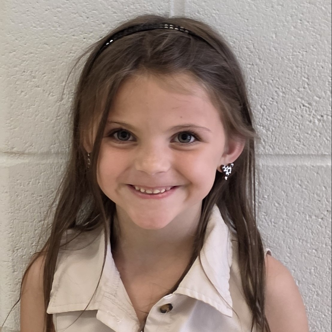 smiling girl with brown hair  pulled back with a headband wearing a tan sleeveless shirt