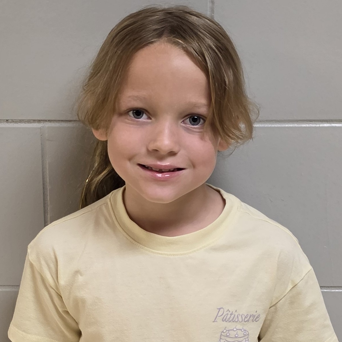 smiling girl with dark blonde hair pulled back wearing a light yellow t-shirt