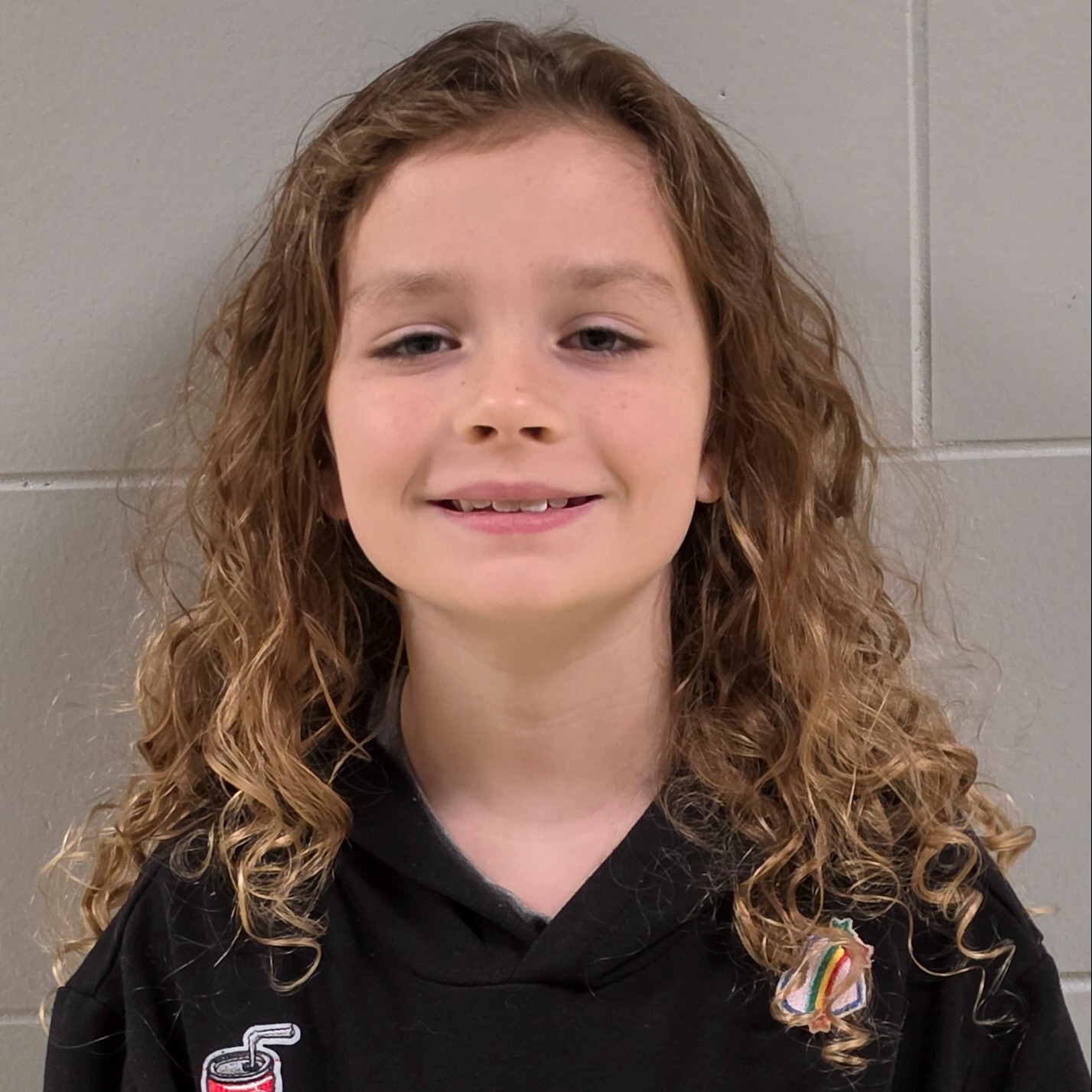 smiling girl with long, dark blonde curly hair wearing a black hooded sweatshirt