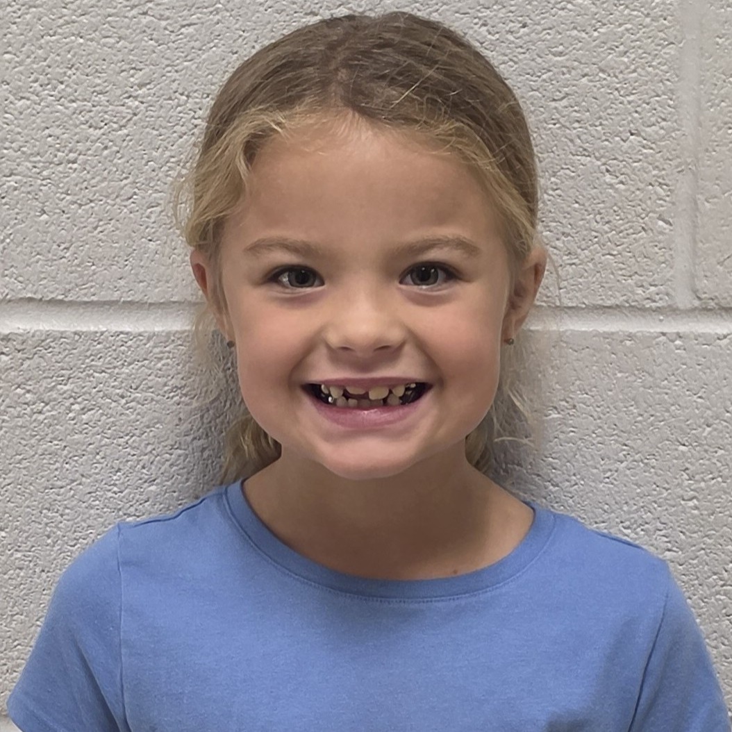 smiling girl with dark blonde hair pulled back wearing a blue t-shirt