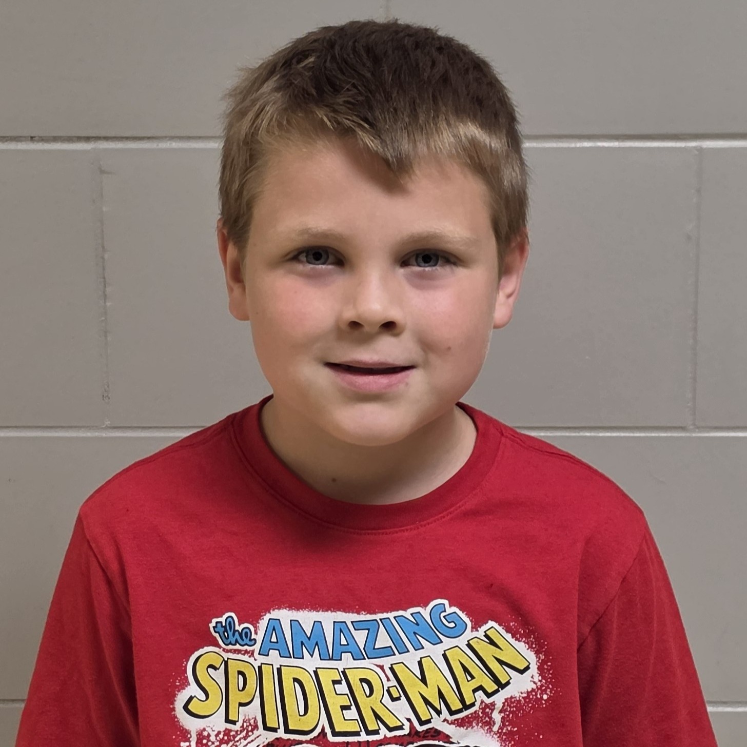 smiling boy with dark blonde hair wearing a red Spiderman t-shirt