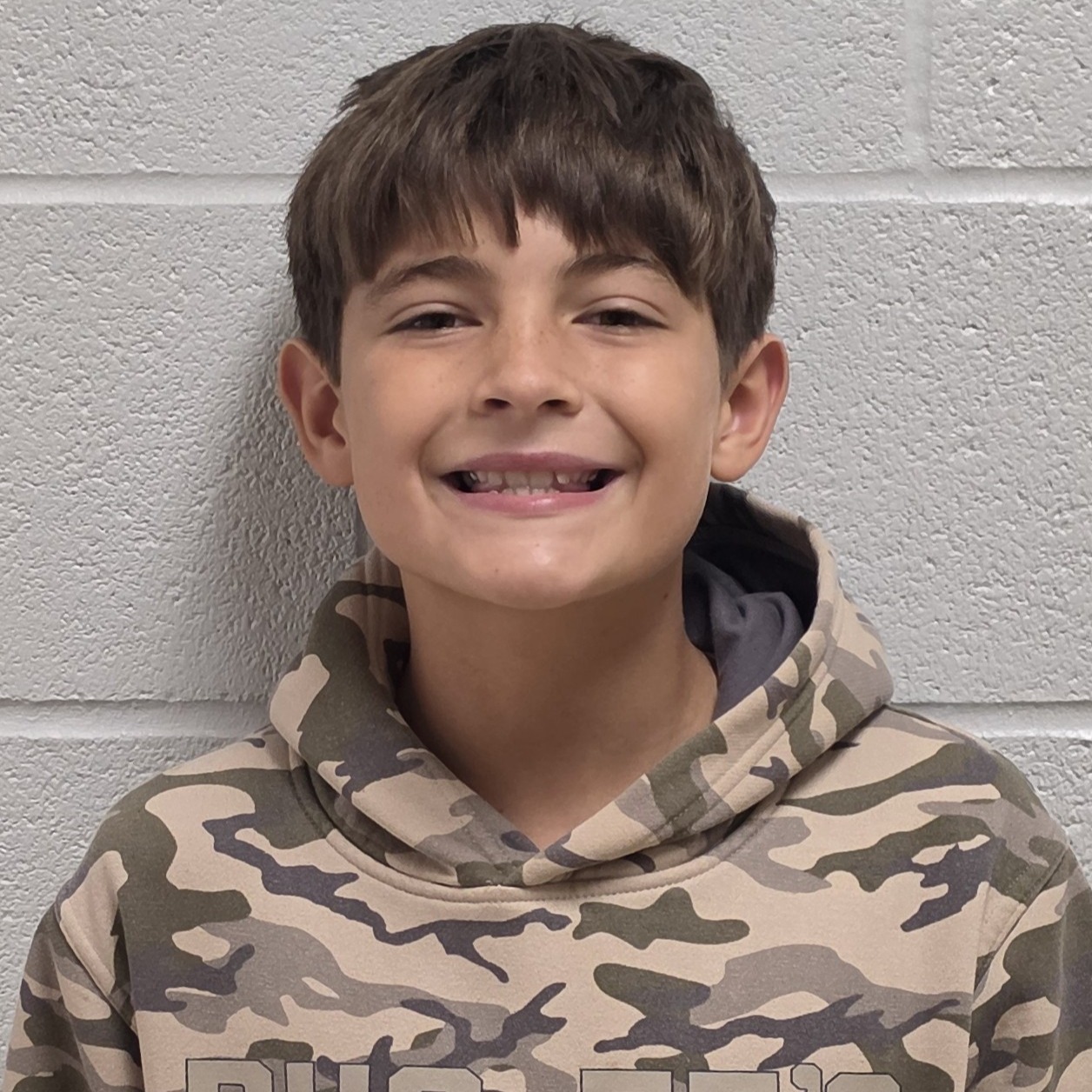 smiling boy with brown hair wearing a camouflage hoodie