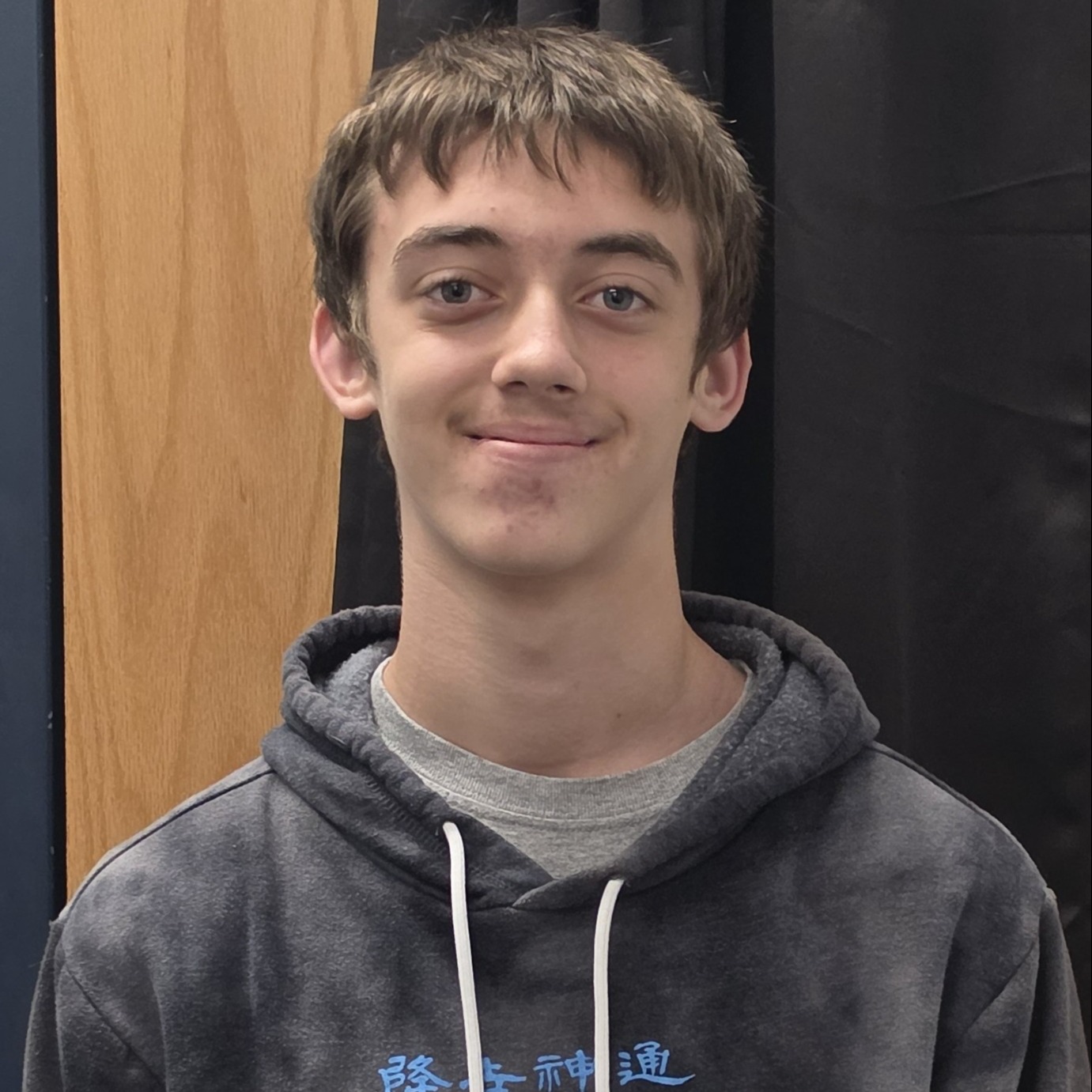 grinning boy with brown  hair  wearing a gray t-shirt under a gray hoodie