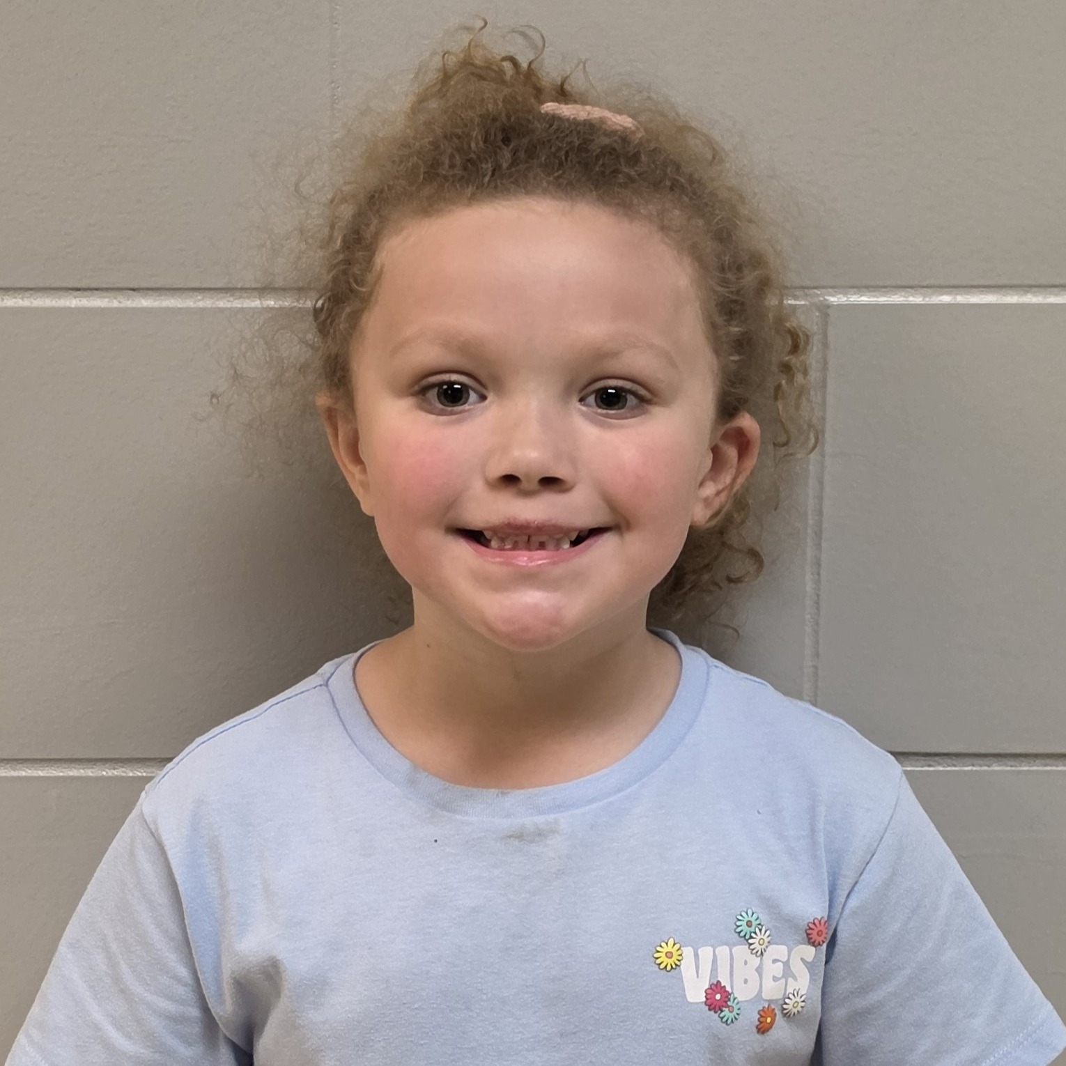 smiling little girl with light brown, curly hair pulled up wearing a light blue t-shirt