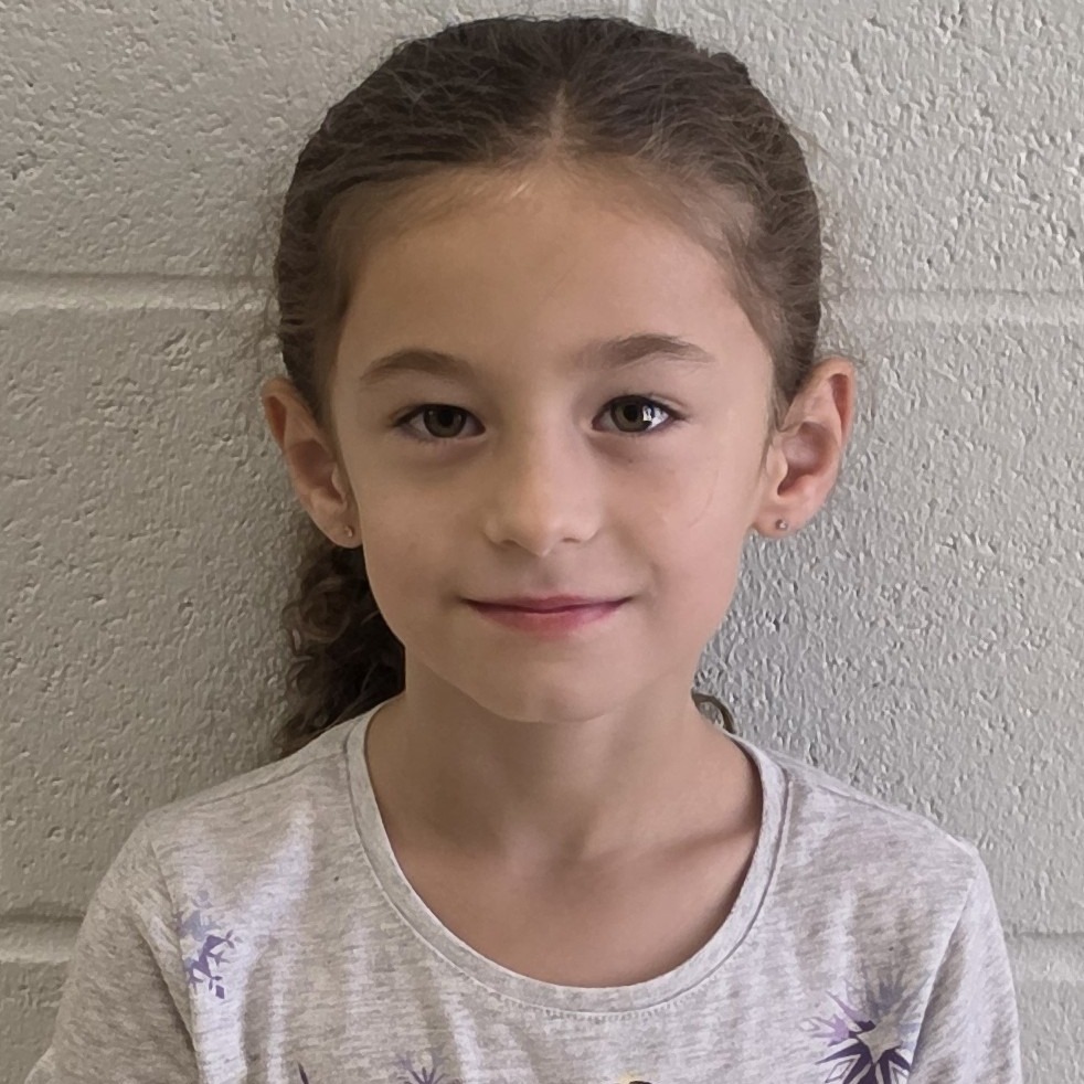 little girl with brown, curly hair pulled up wearing a gray t-shirt