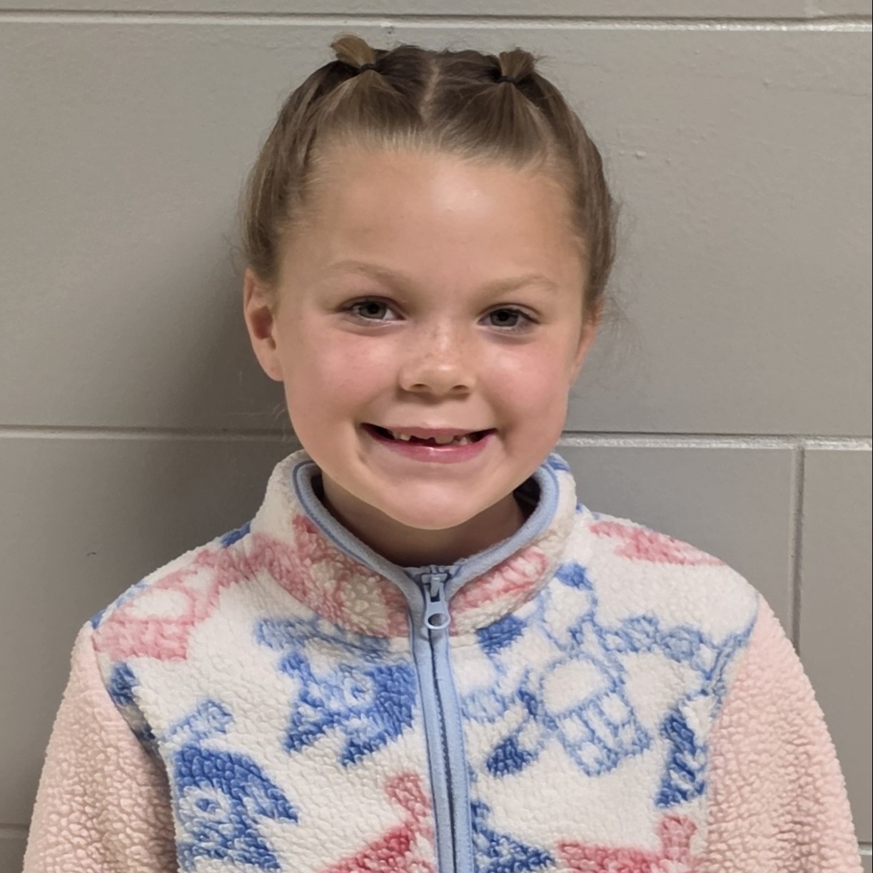 smiling girl with brown hair pulled up wearing a pink & white zipped up sherpa jacket