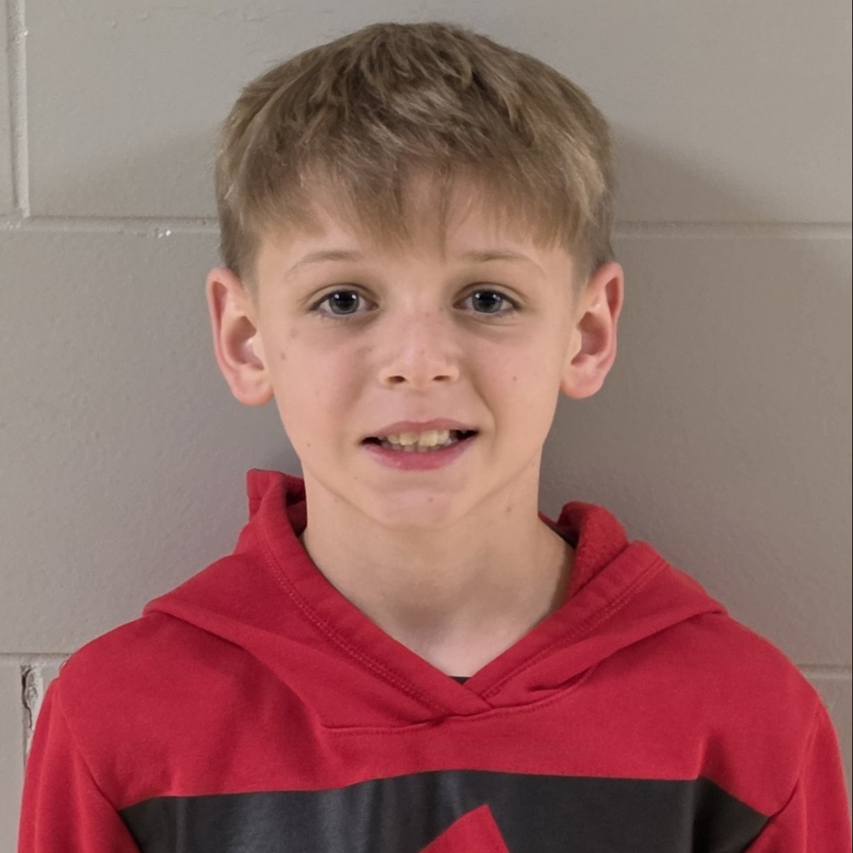 smiling boy with sandy hair wearing a red hooded sweatshirt