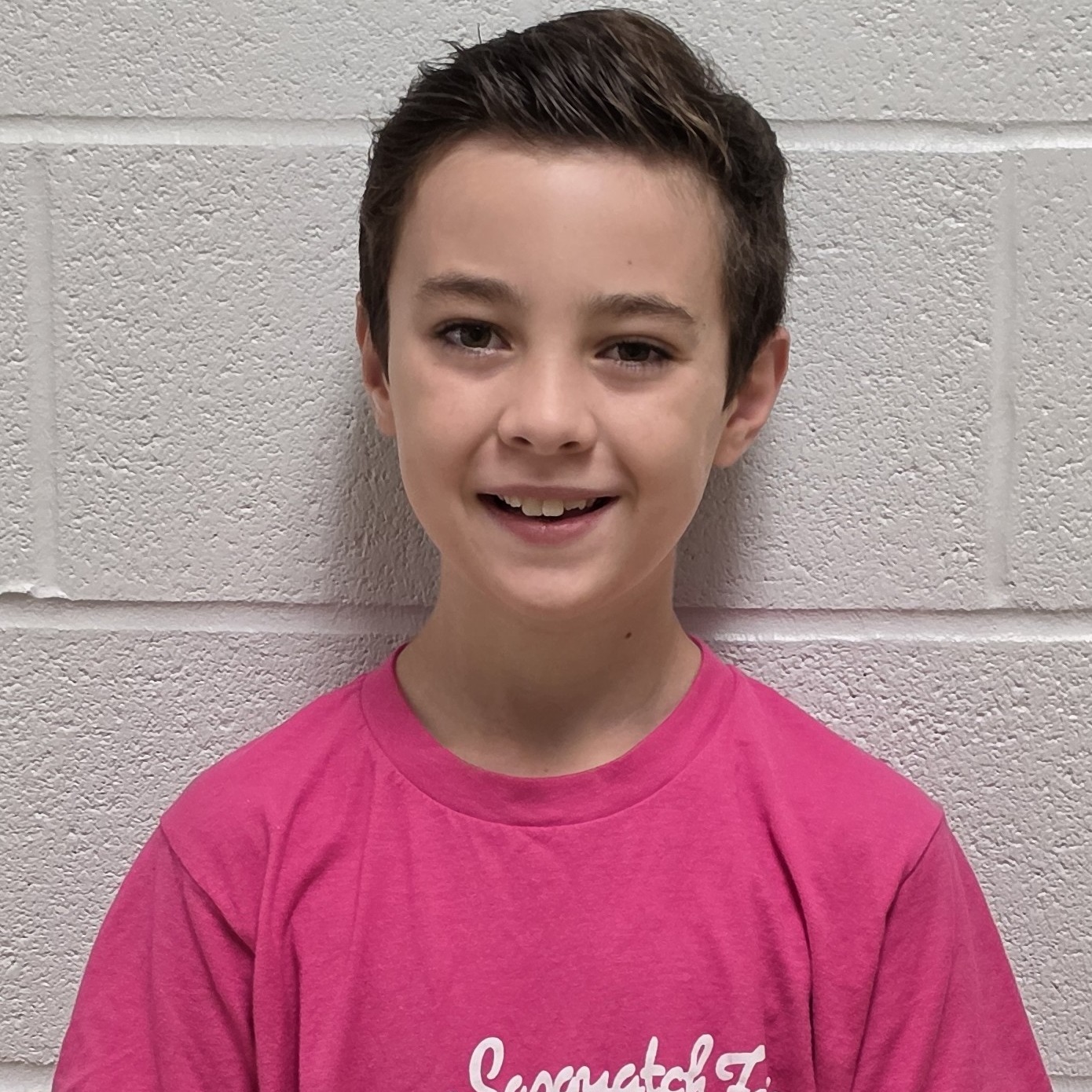 smiling boy with brown hair wearing a pink t-shirt