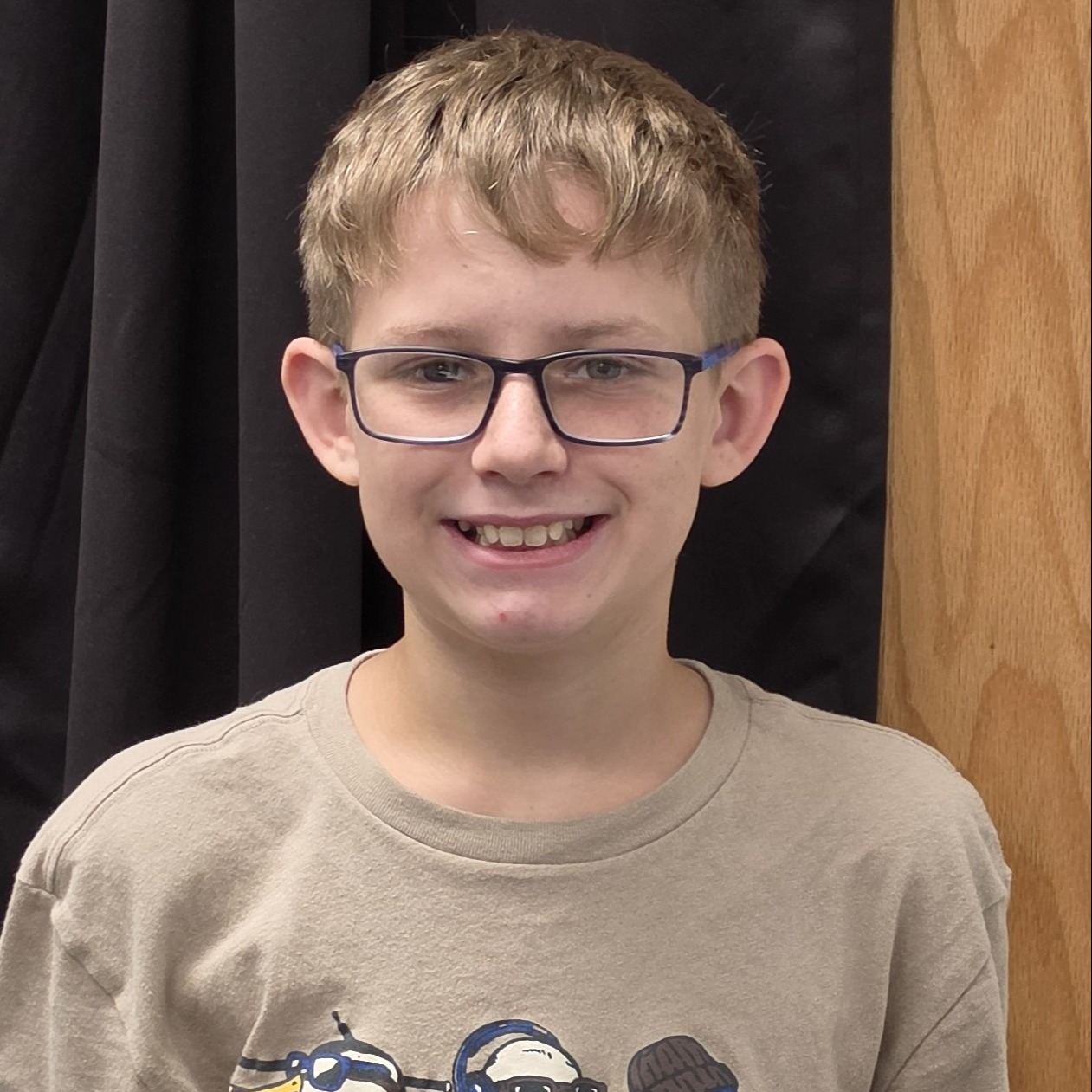 smiling boy with light  brown  hair  wearing a tan t-shirt and glasses