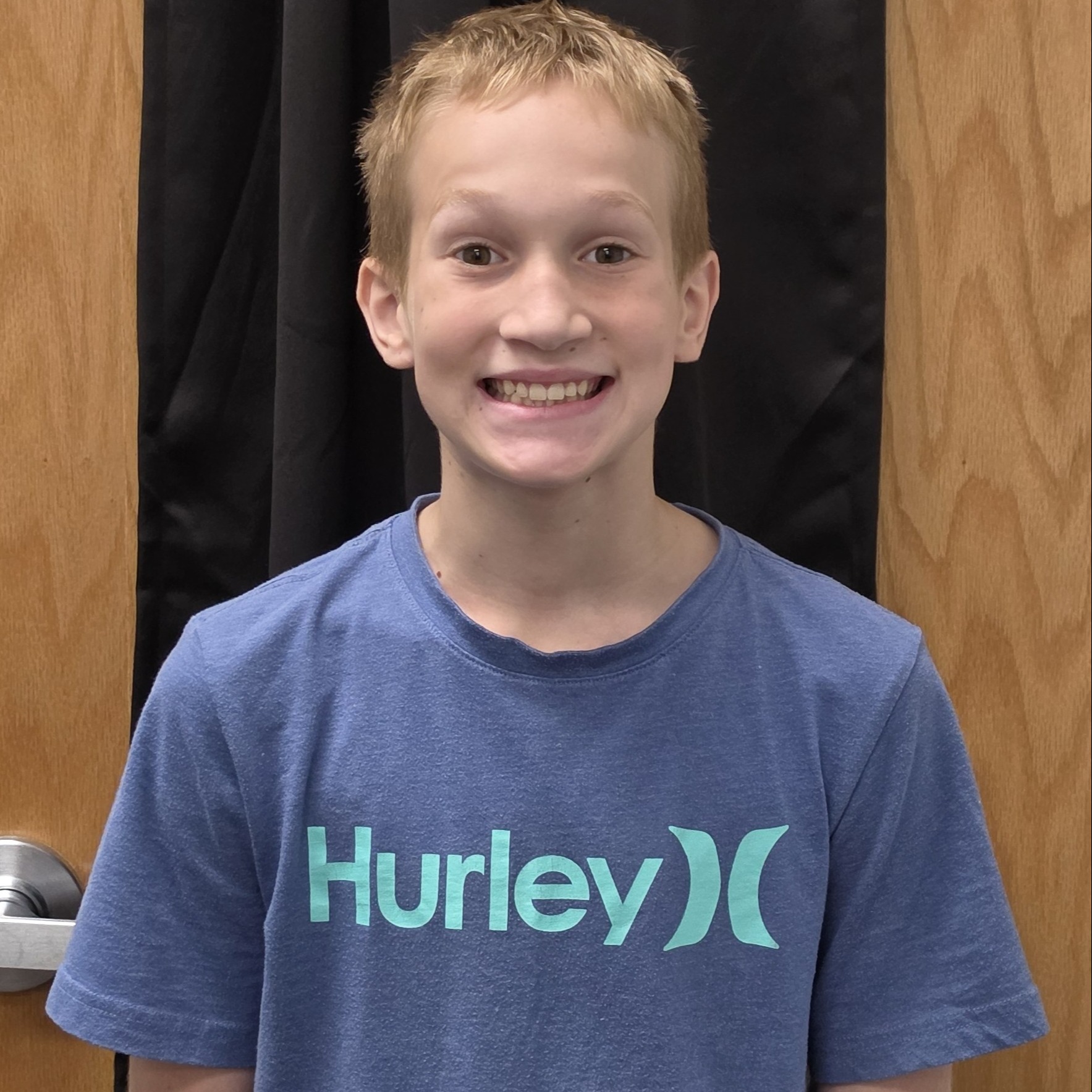 smiling boy with blonde hair wearing a blue t-shirt