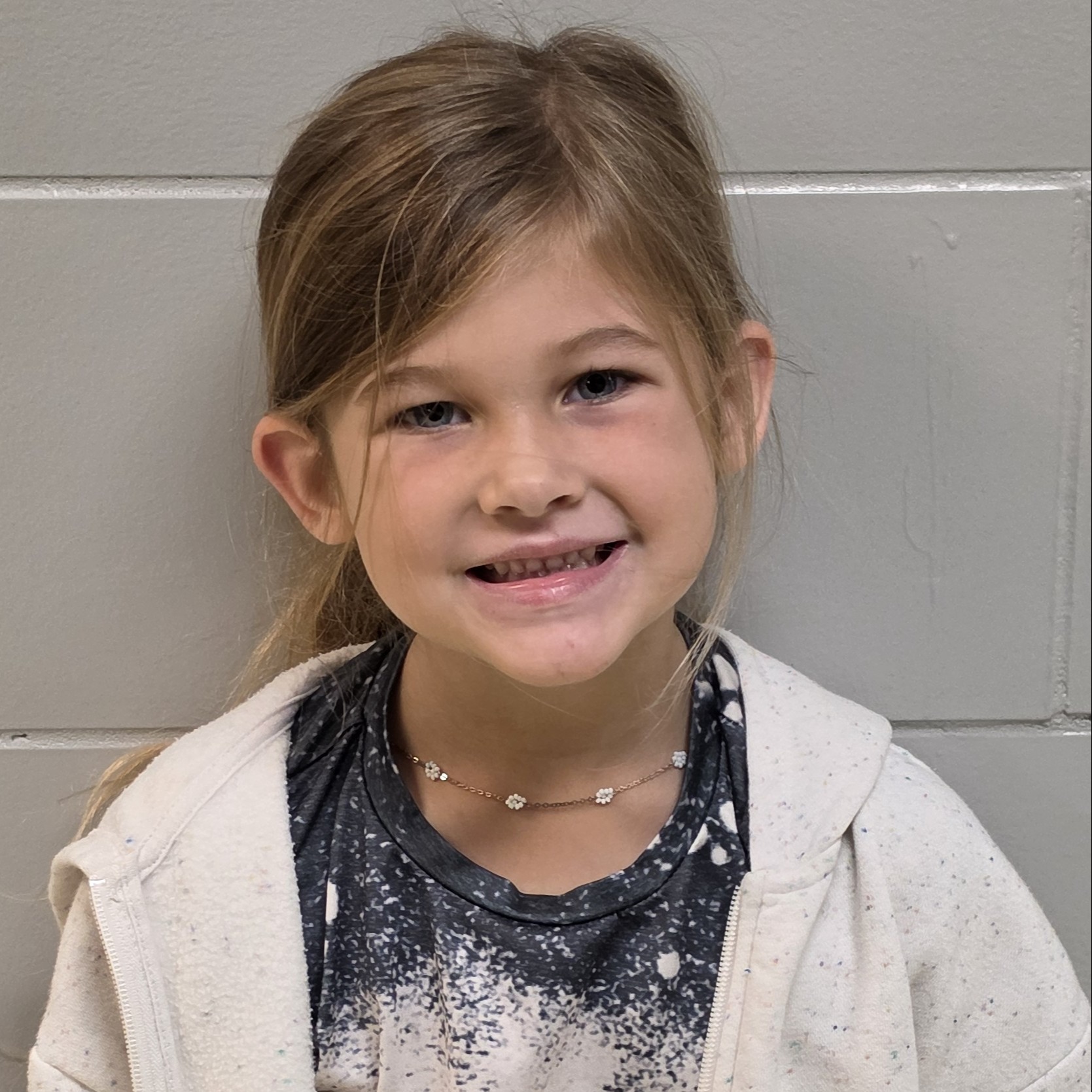 little girl with light brown hair pulled up wearing a gray t-shirt under a white jacket