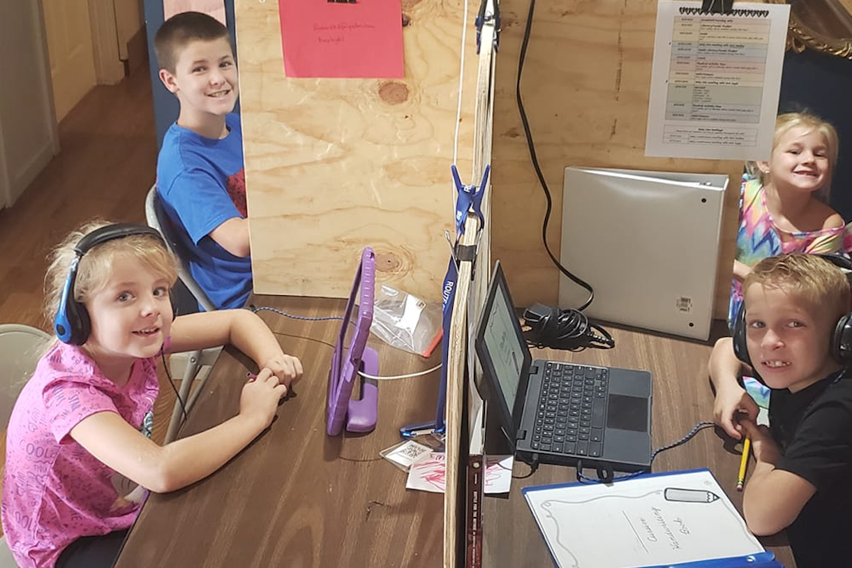 four children sit at homemade dividers working on digital devices