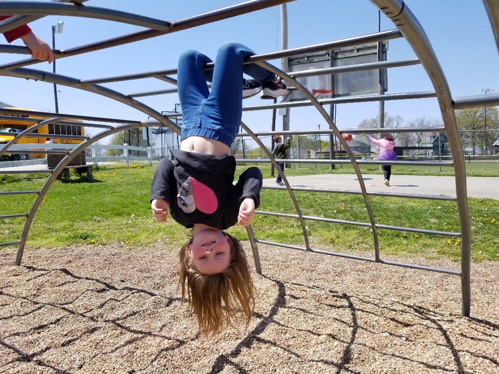 student hanging upside-down from monkey bars