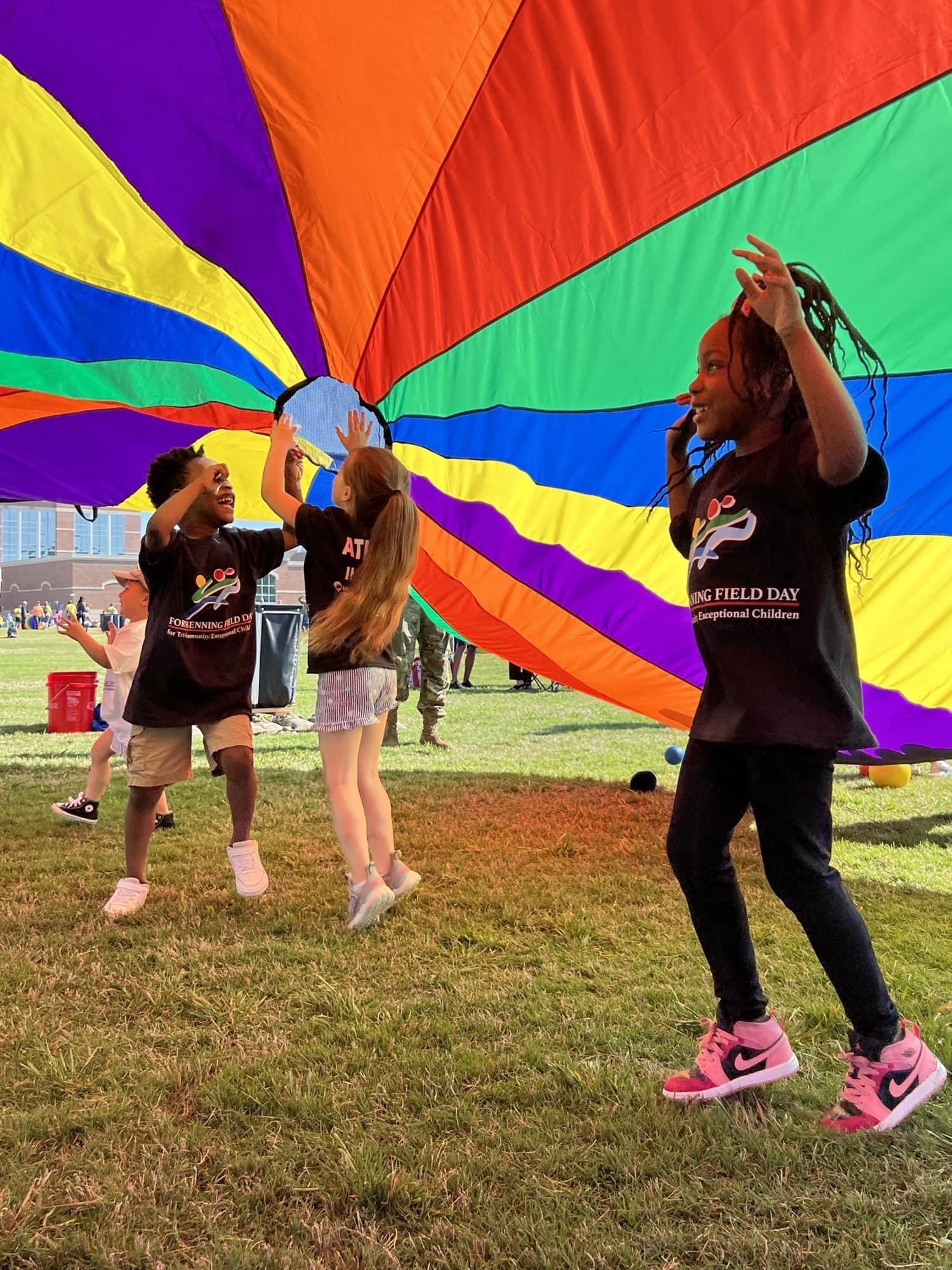 three children playing underneath of colorful parachute