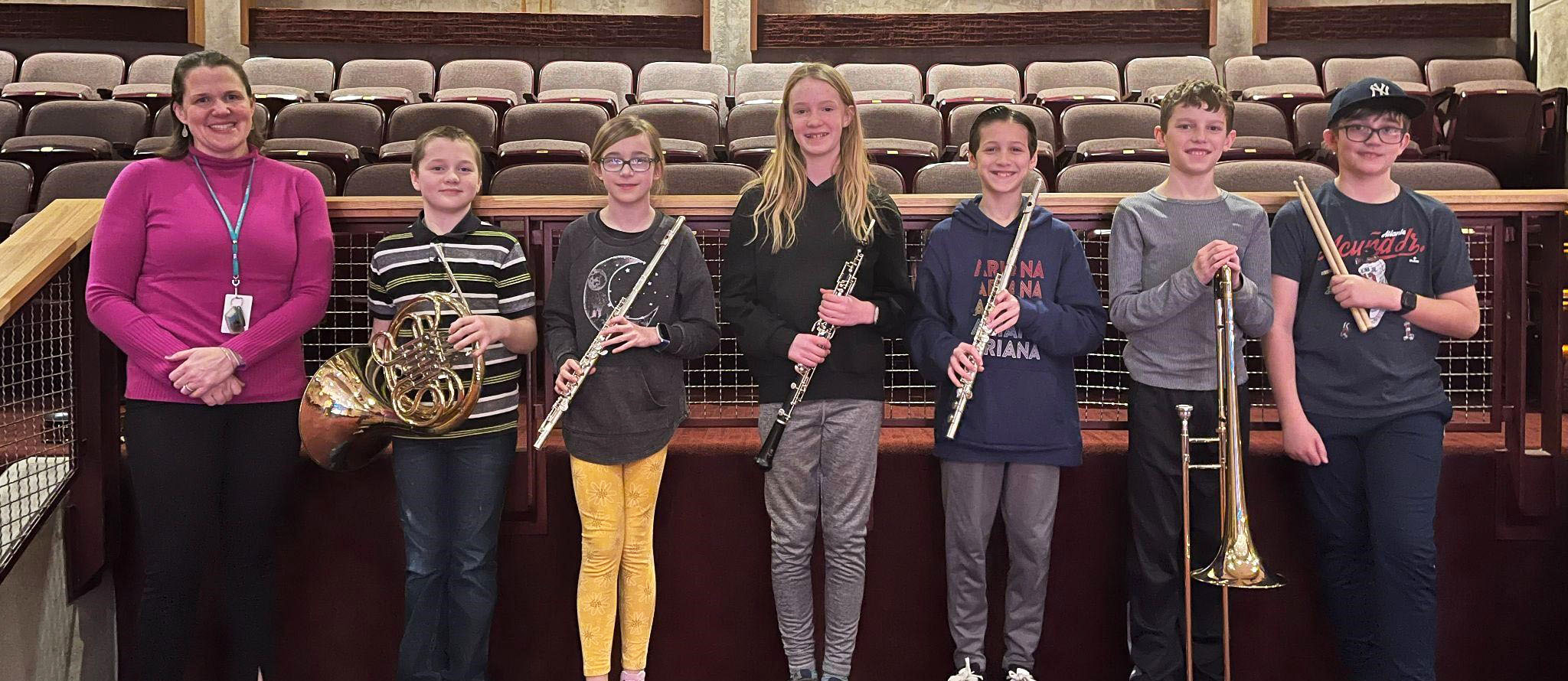Students holding musical instruments next to a teacher