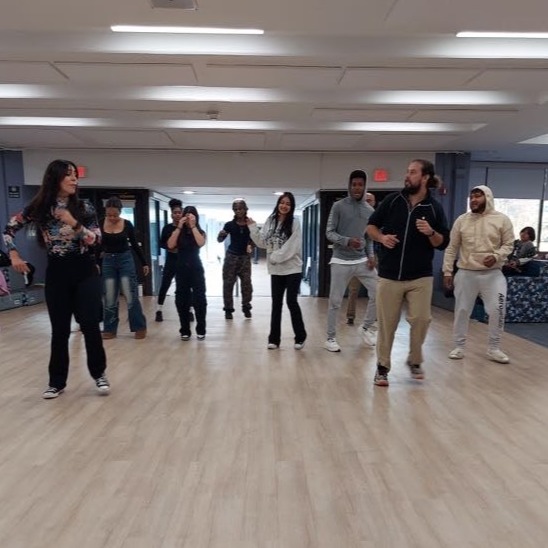 Ms. Ferreira (Phys Ed) leads Mr. Paulsen (Librarian) and students in a Latin Dance Class