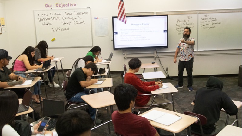 students sitting in a classroom with a teacher standing up front