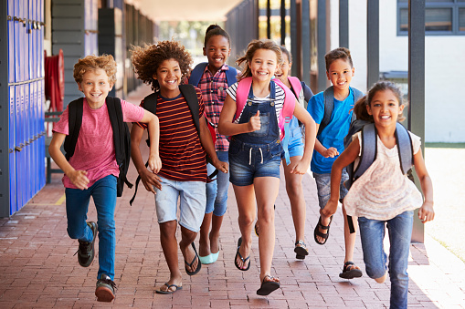 7 kids with backpacks running down walkway