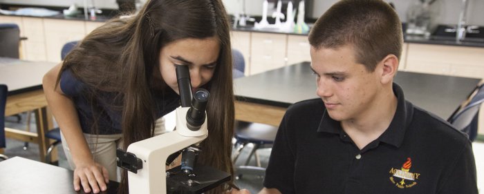 two students, one looking through a microscope