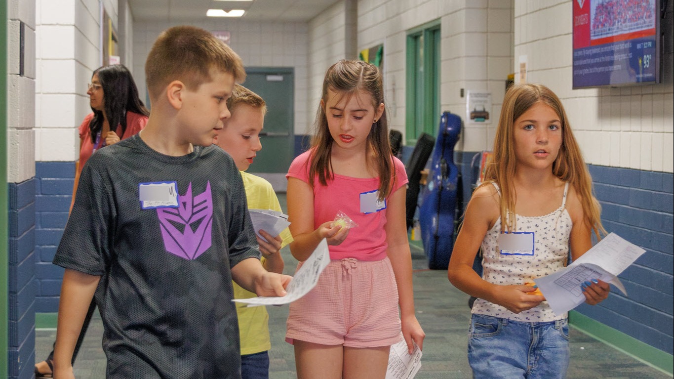 four students walking down the hallway with papers in their hands