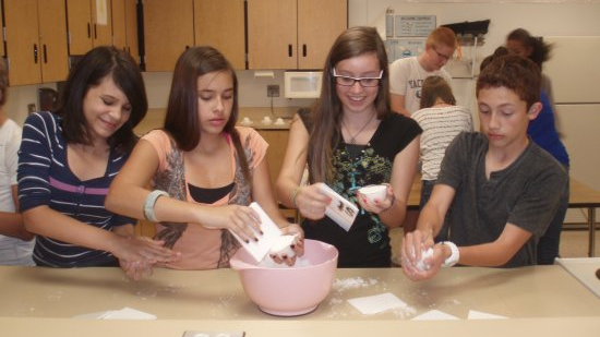 four students adding cooking ingrediants to a bowl