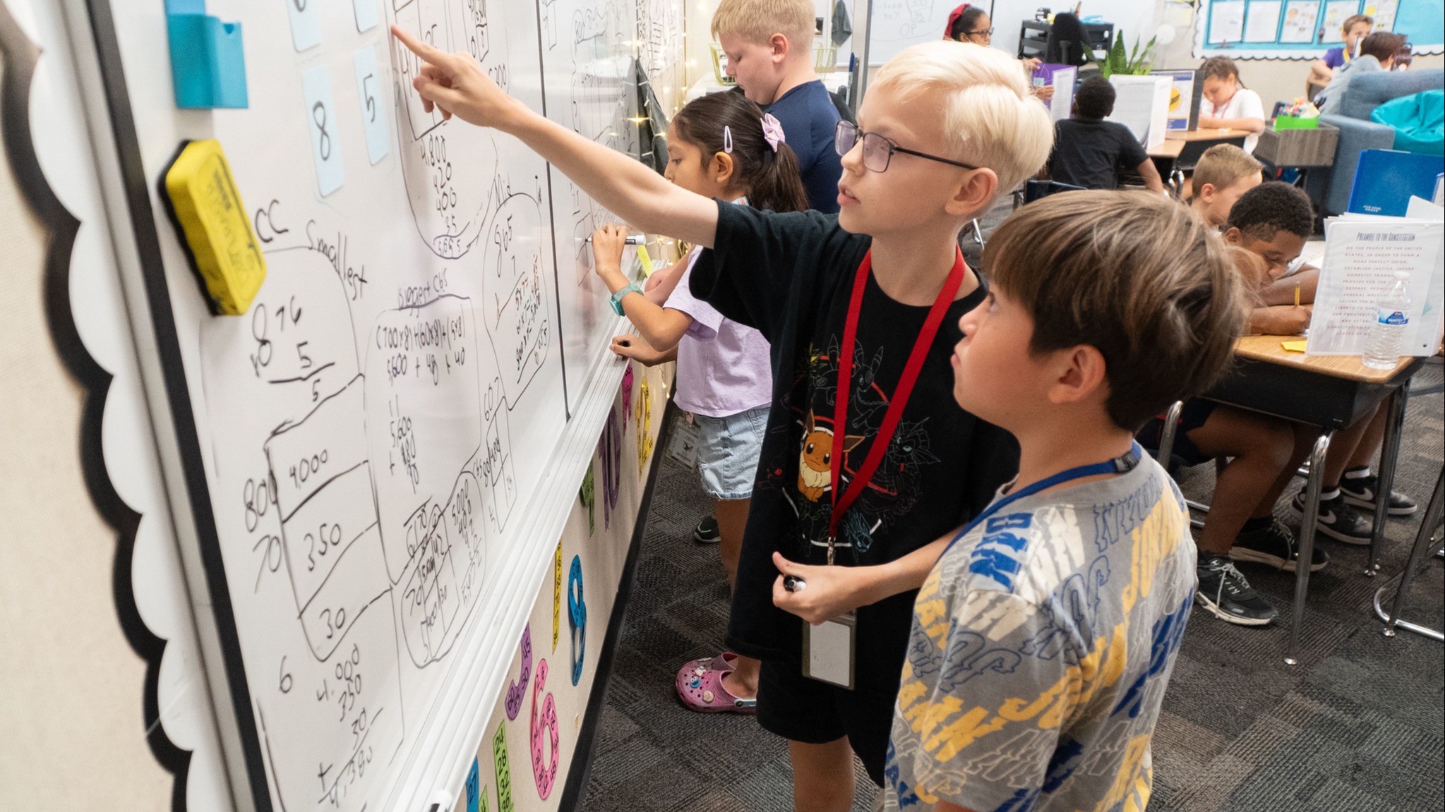 Stuldents standing at a white board working on problems