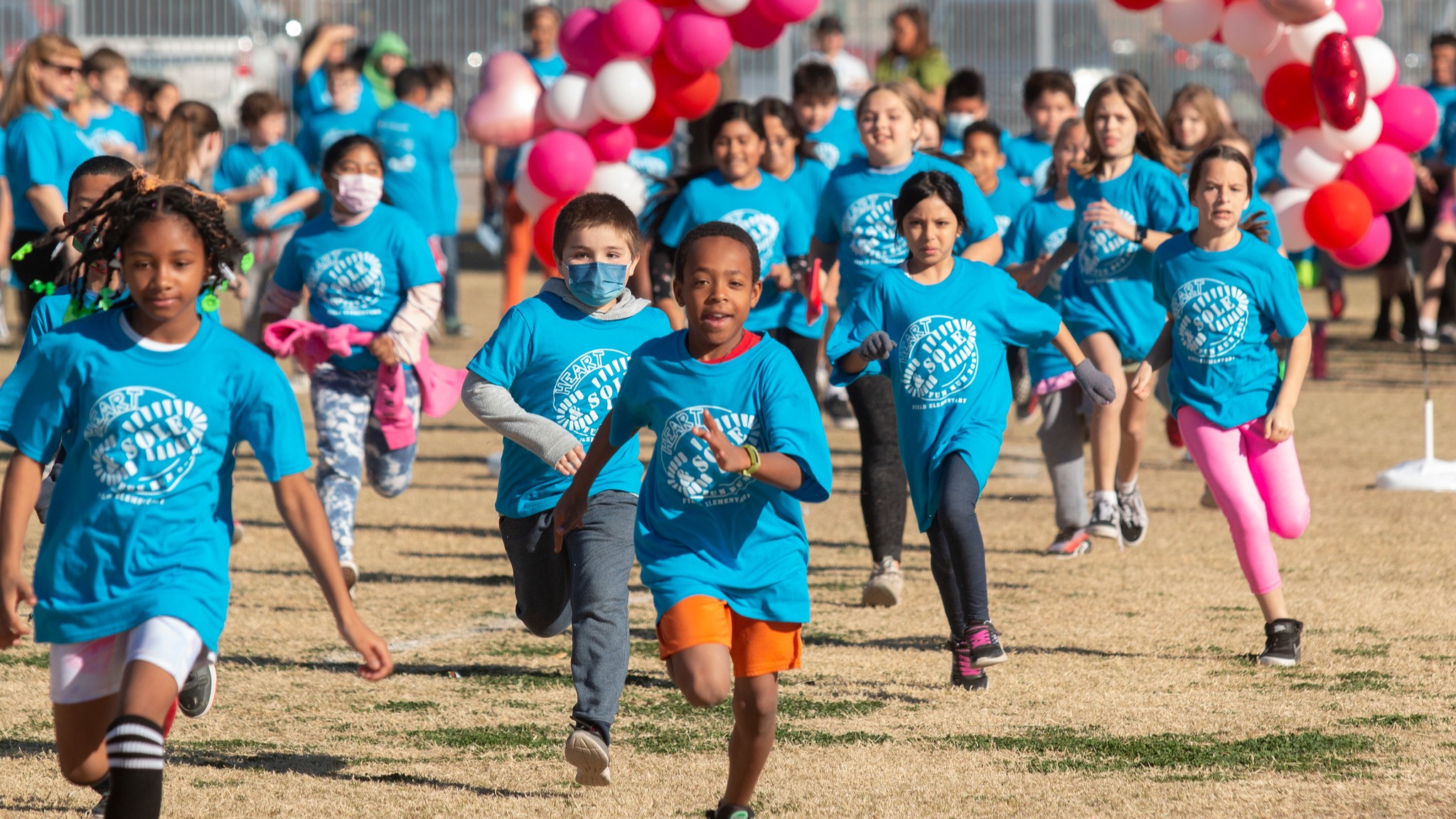 students running on a playground with a balloon arch behind them