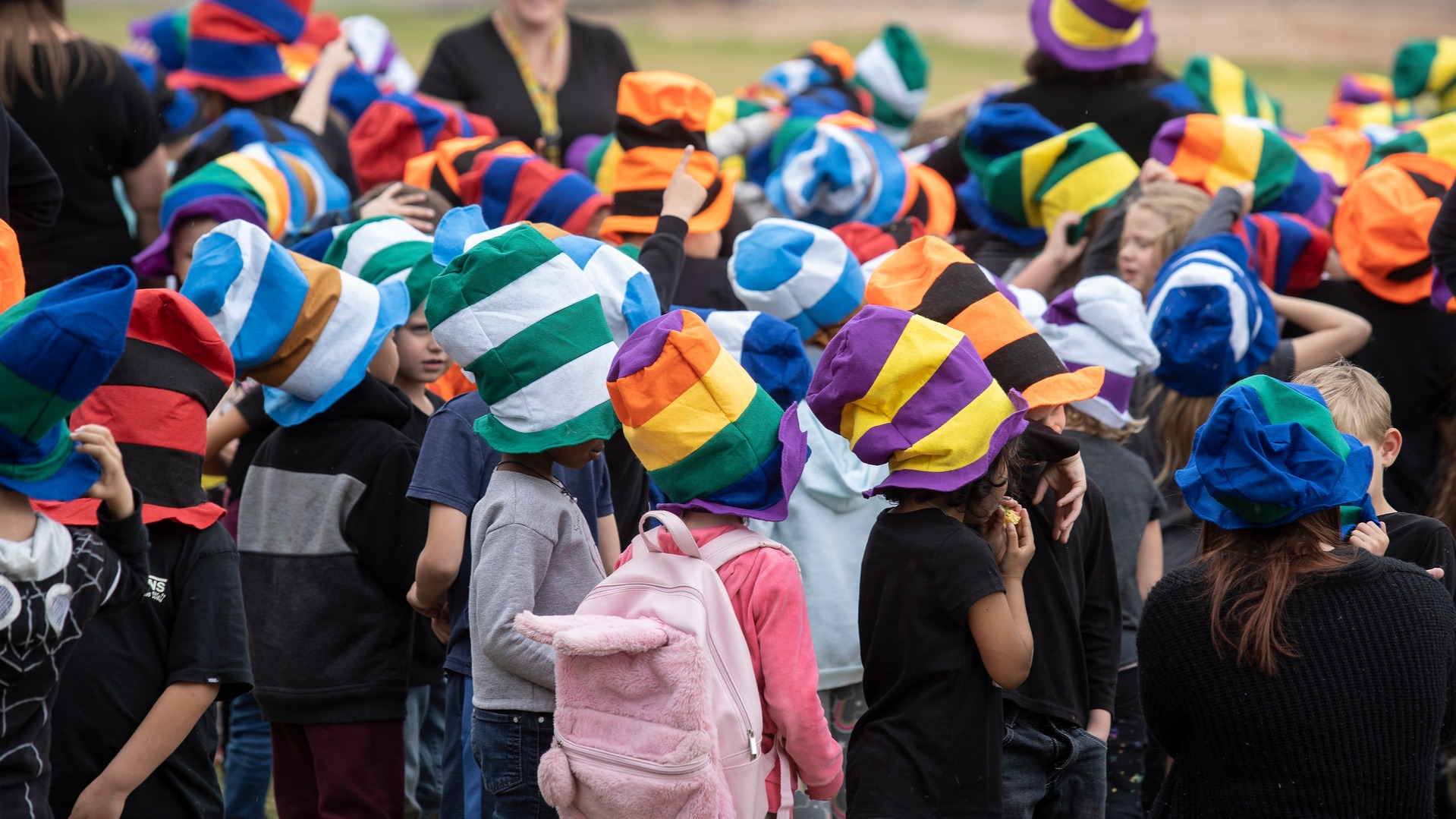 stuldents standing on a playground, all with colorful Dr. Seuss hats