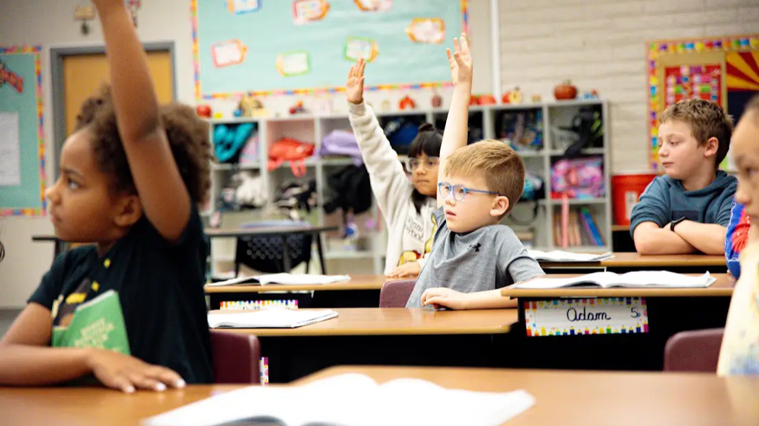 5 students sitting in a classroom, 3 have their hands up