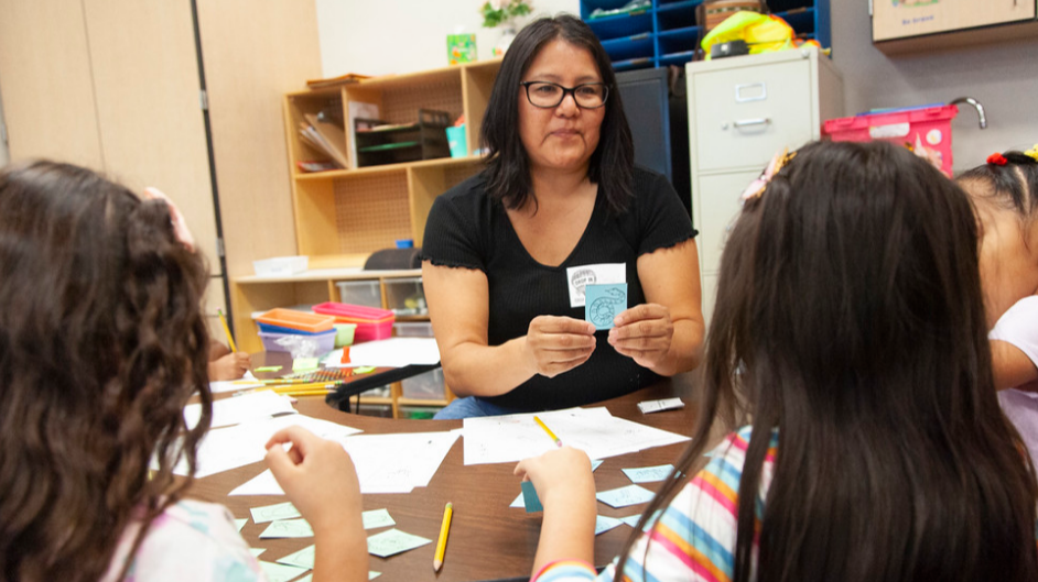 teacher sitting with students at table showing them flashcards