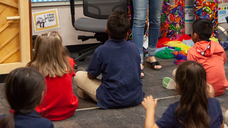 five students sitting on the floor watchin the teacher