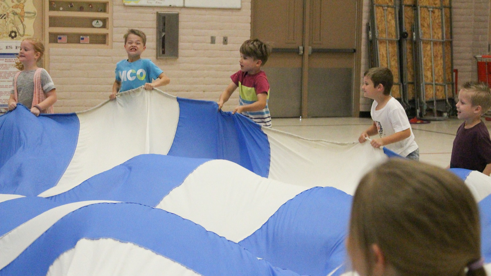 six students holding the sides of a parachute in the gym