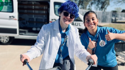 two students , one on bike with blue hair the other with two thumbs up