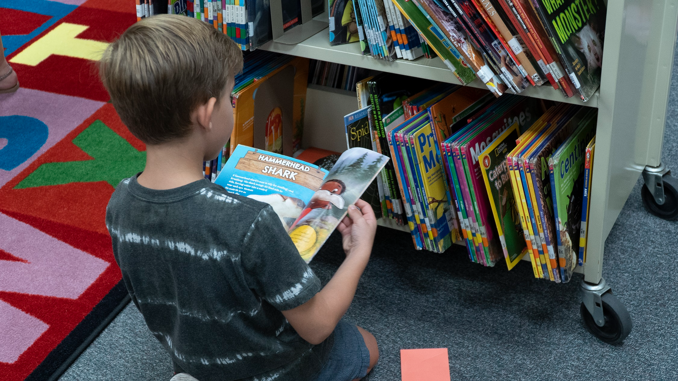 student sitting on floor looking at books on a cart