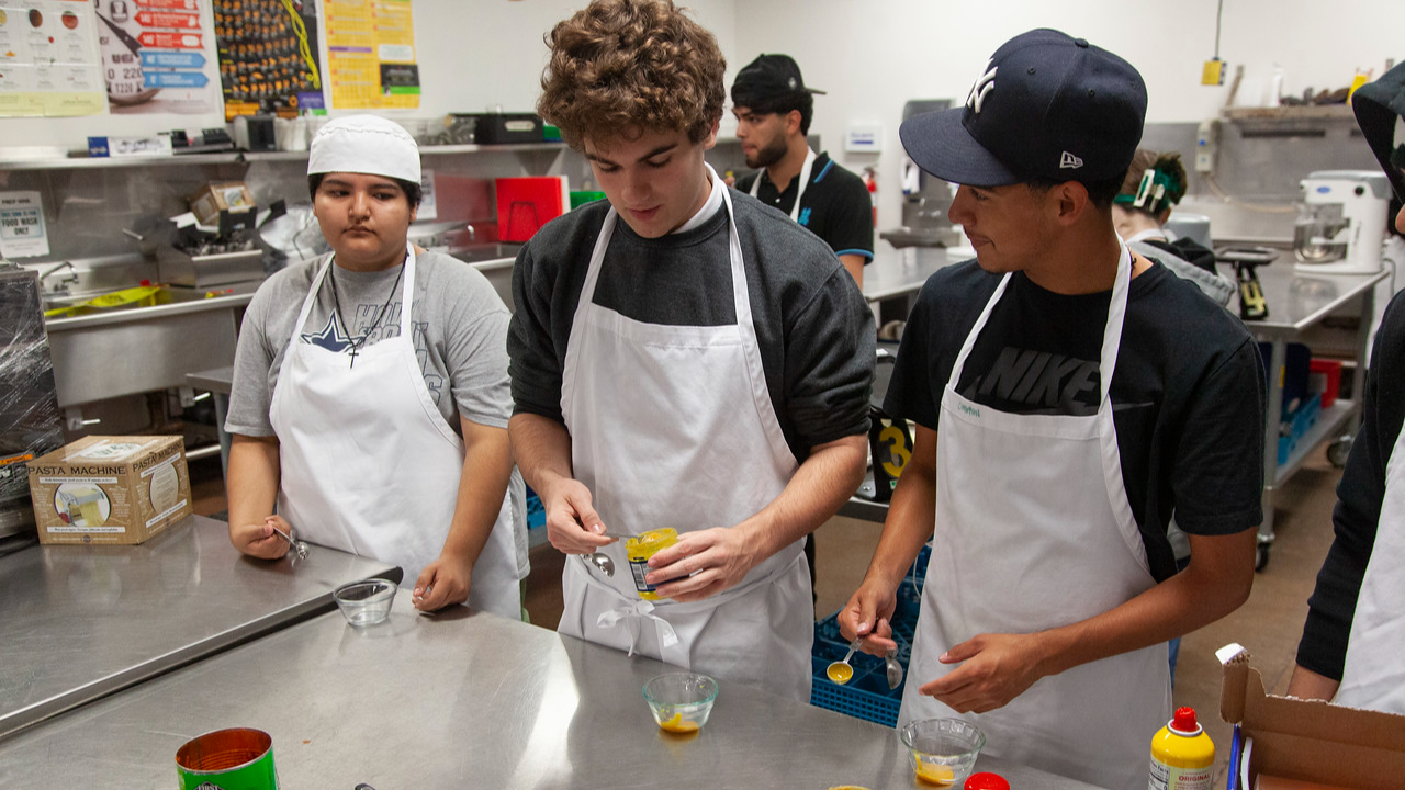 3 students wearing aprons in a kitchen