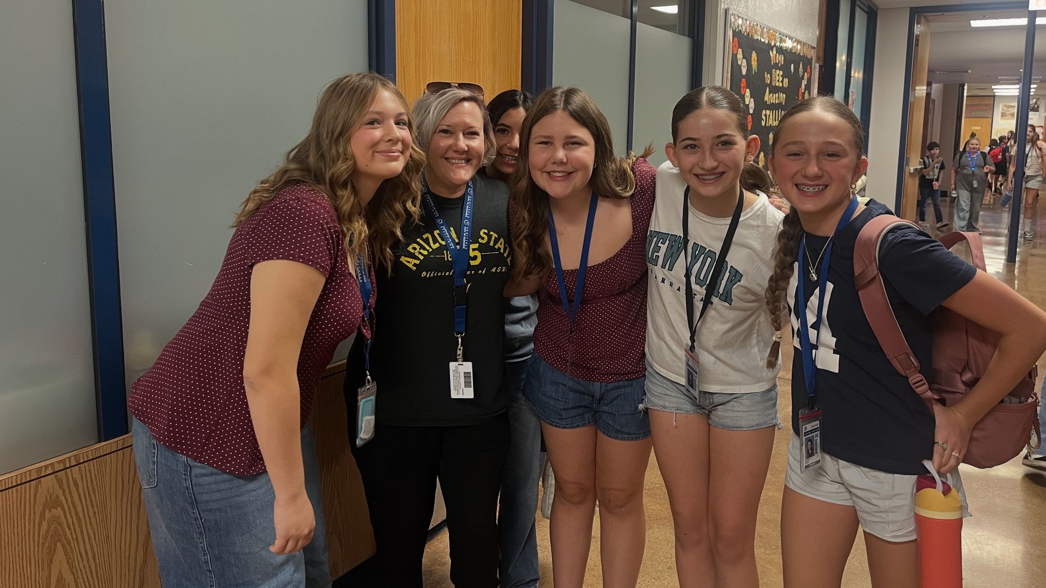 Two teachers and 4 students with their arms around each other standing in a hallway