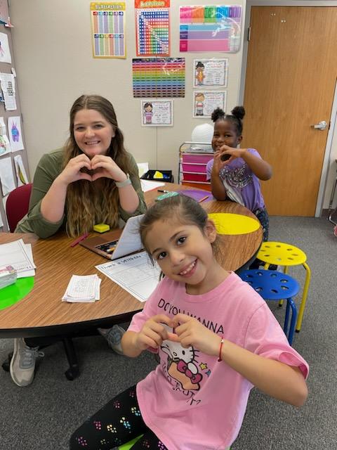 2 students making heart hand gestures 