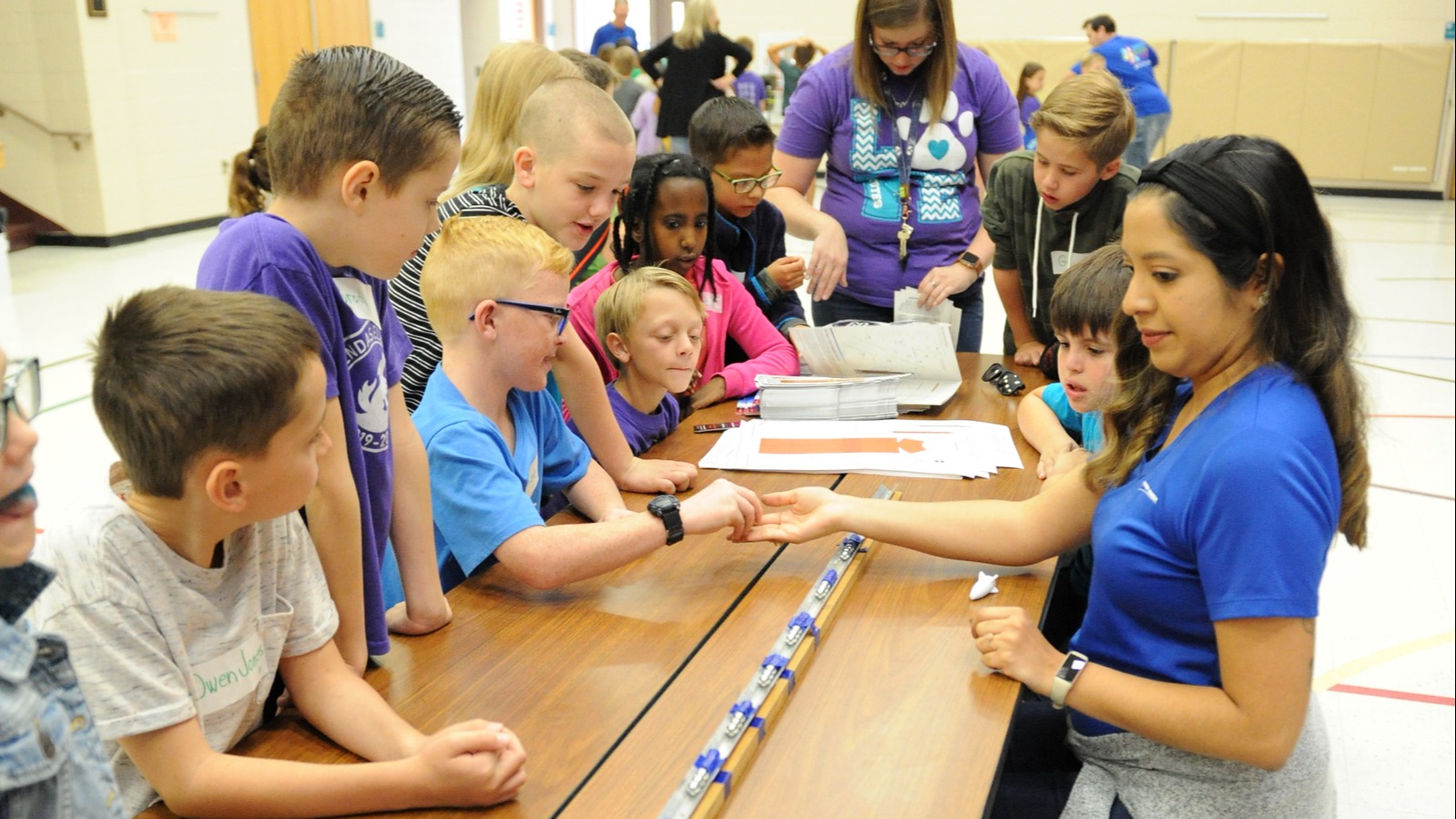 students standing around a table working on a project with 2 teachers