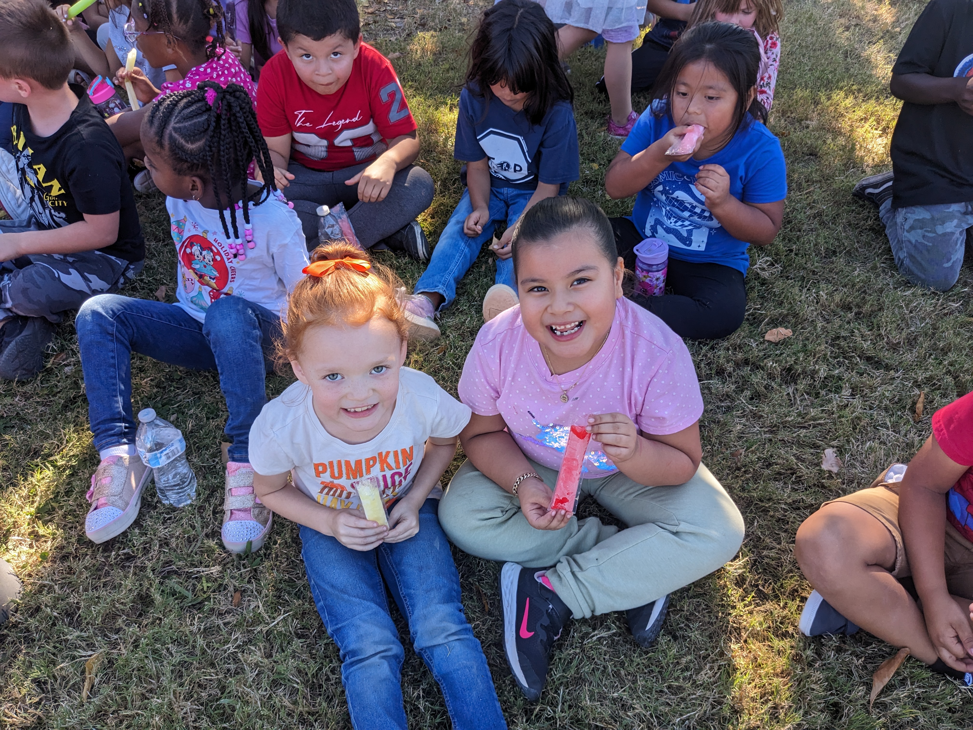 A group of first graders, with two girls at the center, eating Otter Pops