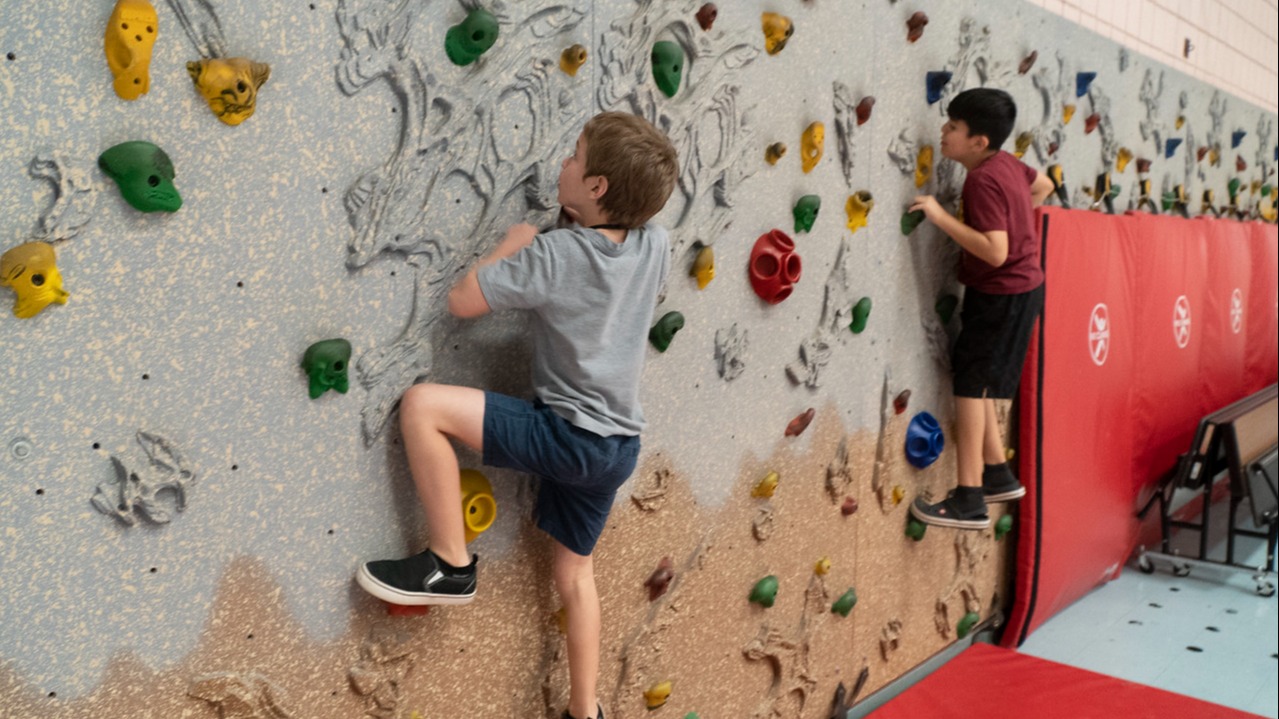 two students climbing rock climbing wall