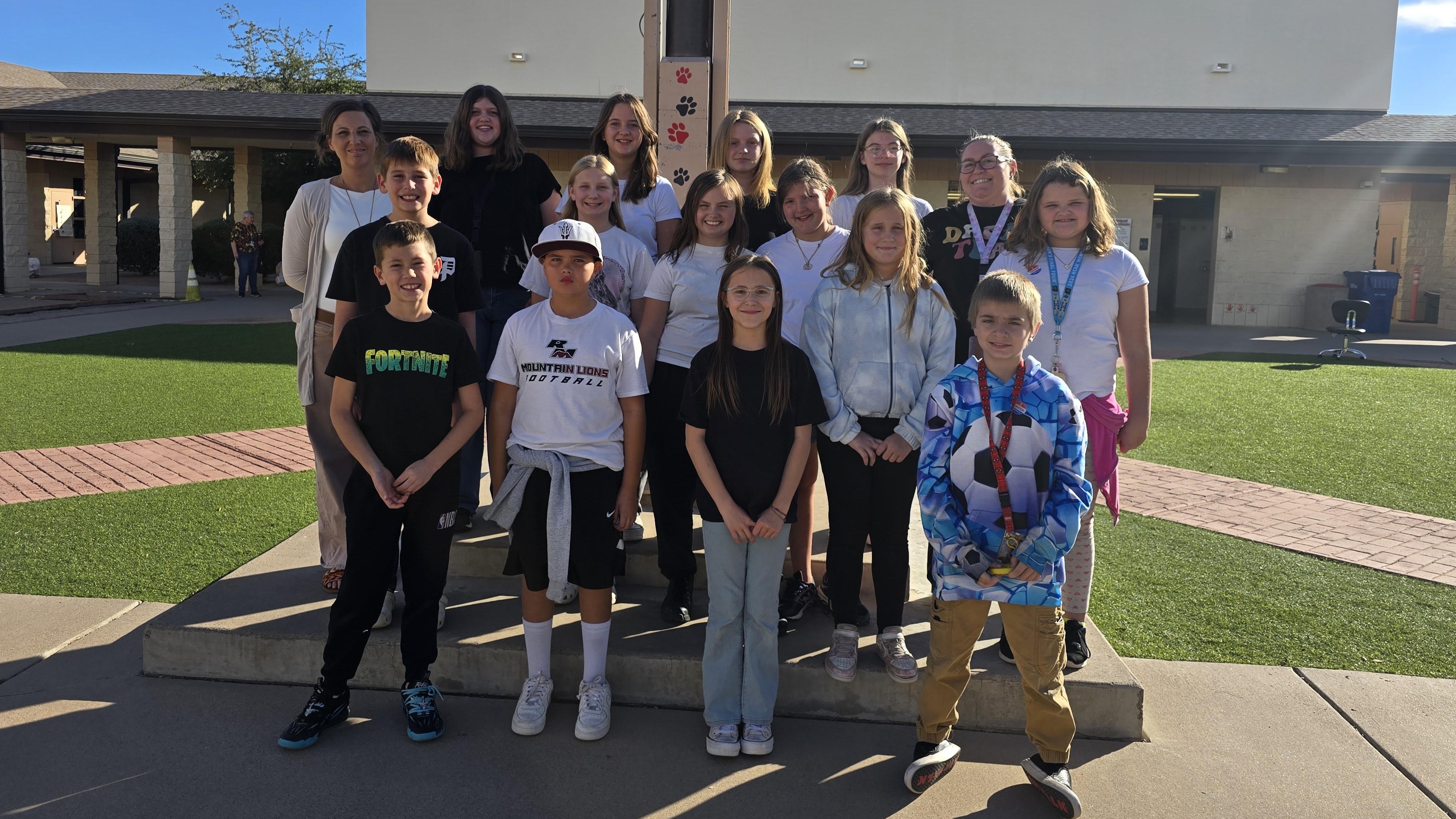 sixteen students standing together in fornt of the school