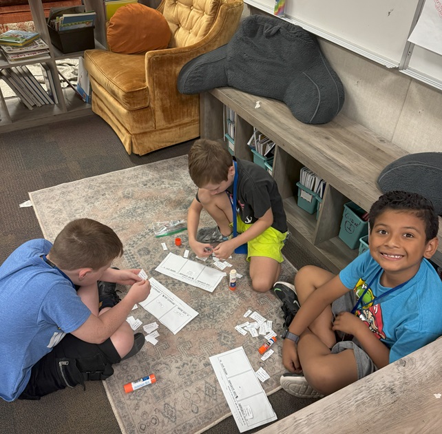 Three third-grade students are working on a project on the floor.