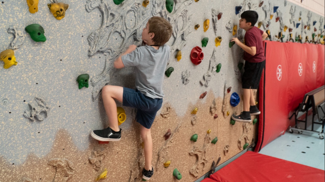 two students climbing rock climbing wall