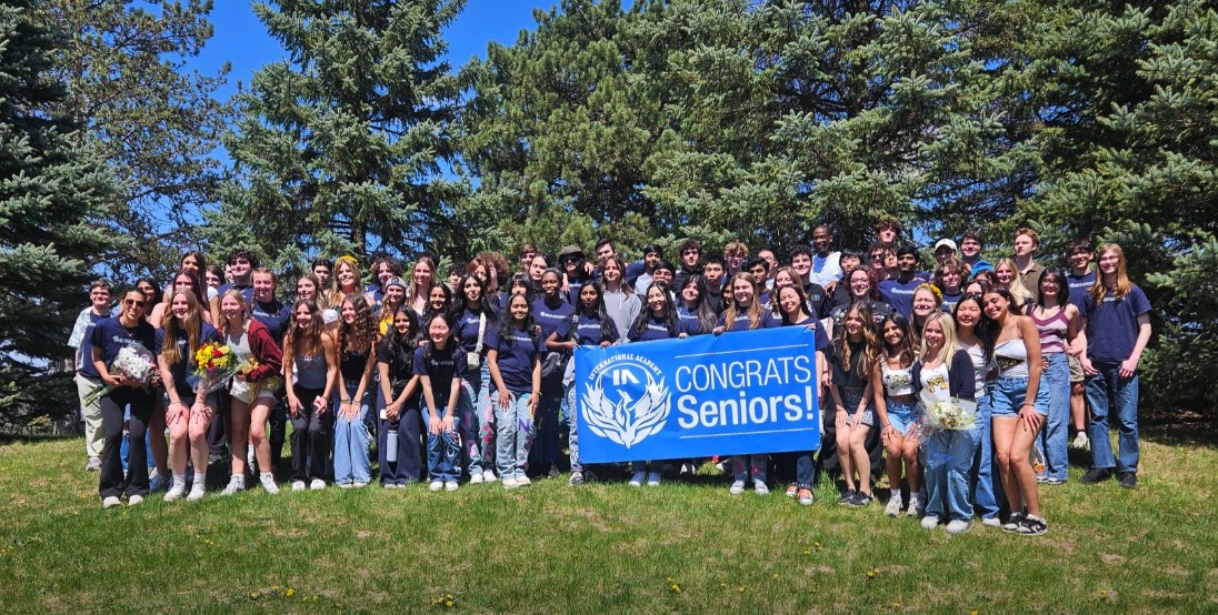 photo of dozens of students smiling outside holding a banner that reads "congrats seniors!"