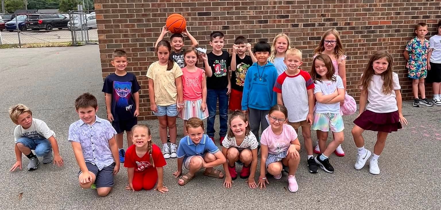 several kids smiling and posing for a photo outside a school