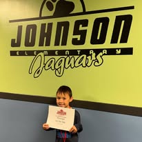 Student holds certificate while posing for photo in from of johnson mural inside school